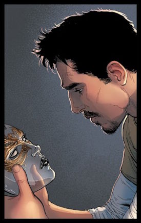 Tony Stark sits forlornly, staring into the eyes of Madame Masque's mask. In the back, his thumb is visible through the surface.